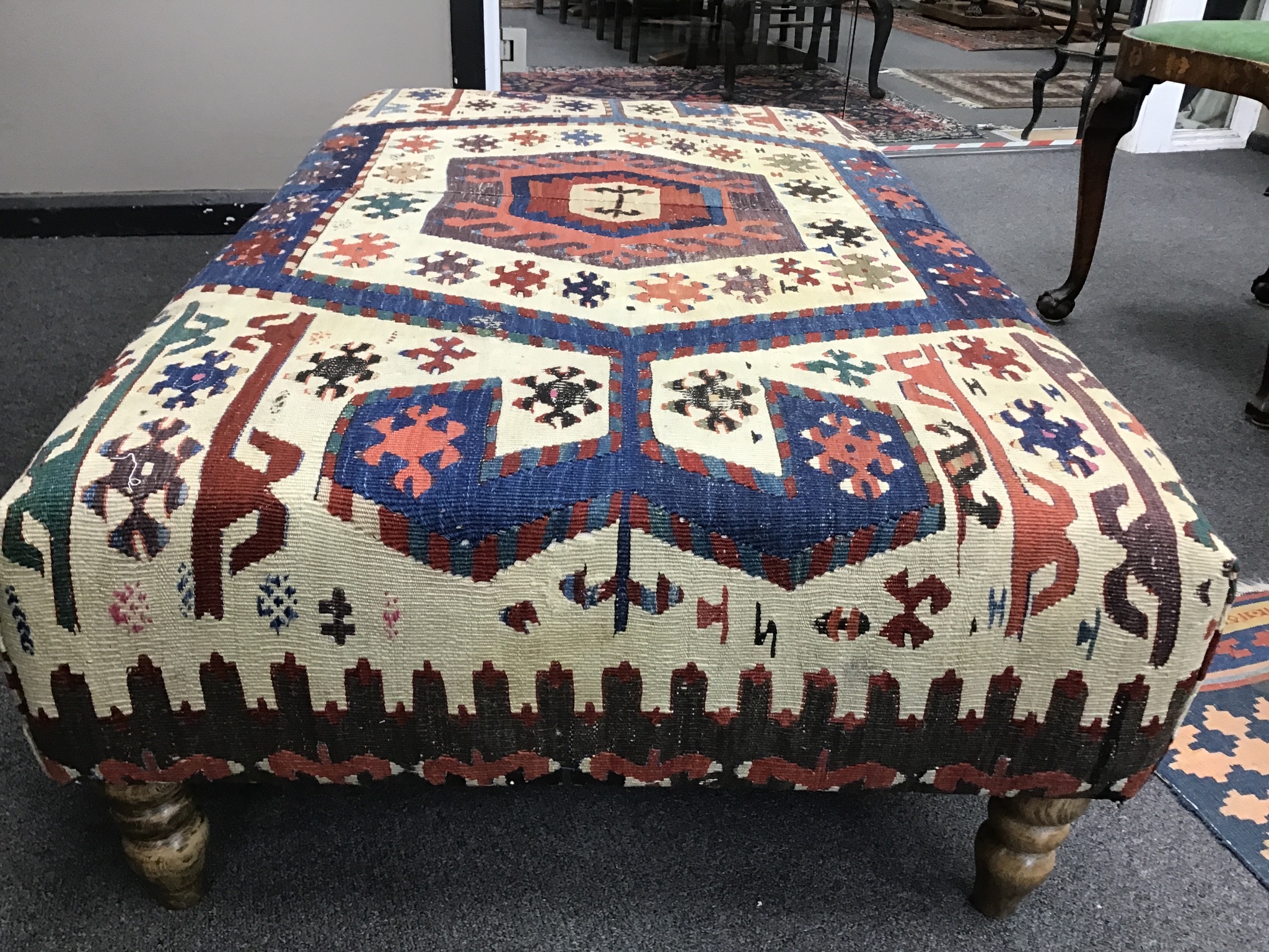 A large rectangular coffee table / footstool with antique kelim upholstery on stained turned beech feet, width 124cm, depth 72cm, height 38cm.